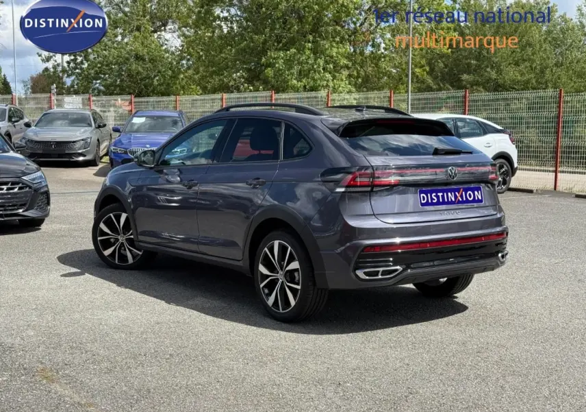 Volkswagen Taigo gris Ascot en 3/4 arrière droit, avec jantes alu et barres de toit visibles sur parking.
