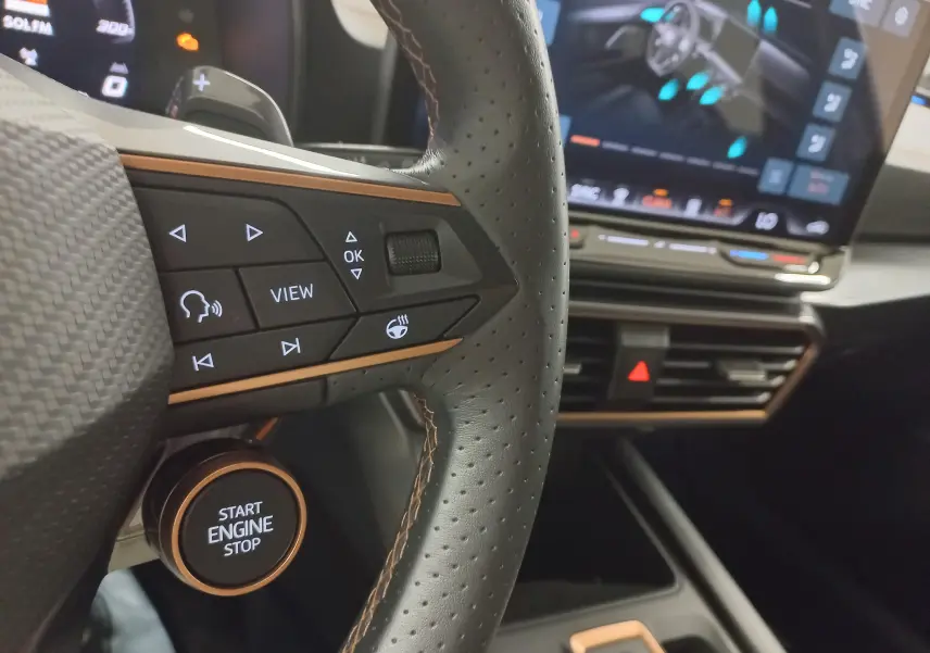 Gros plan sur le volant cuir perforé avec commandes multifonctions et bouton start/stop de la CUPRA Leon 2025.