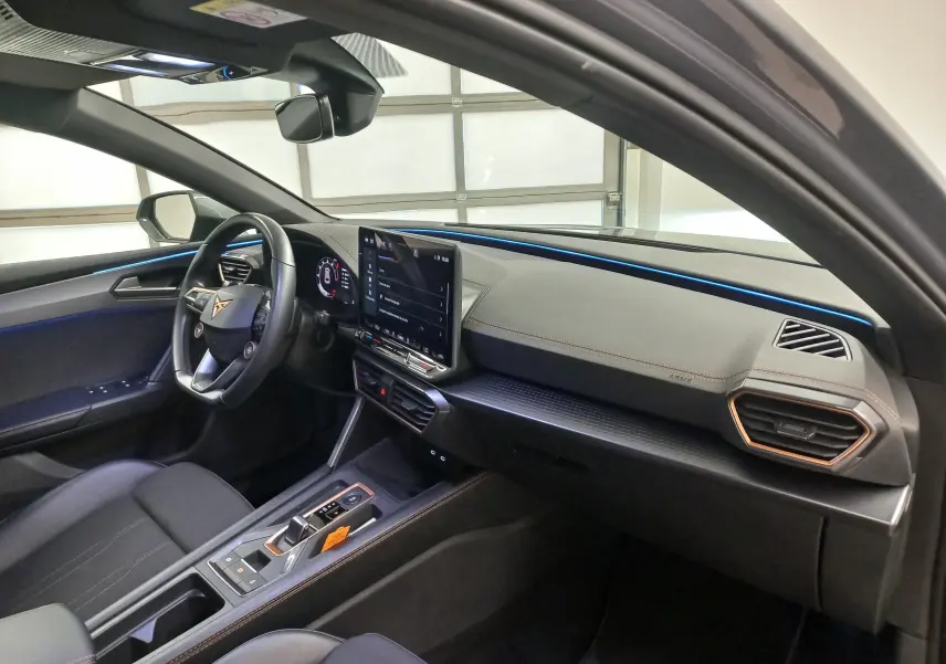 Vue intérieure côté conducteur de la CUPRA Leon Phase 2 avec éclairage d’ambiance bleu et finitions modernes.