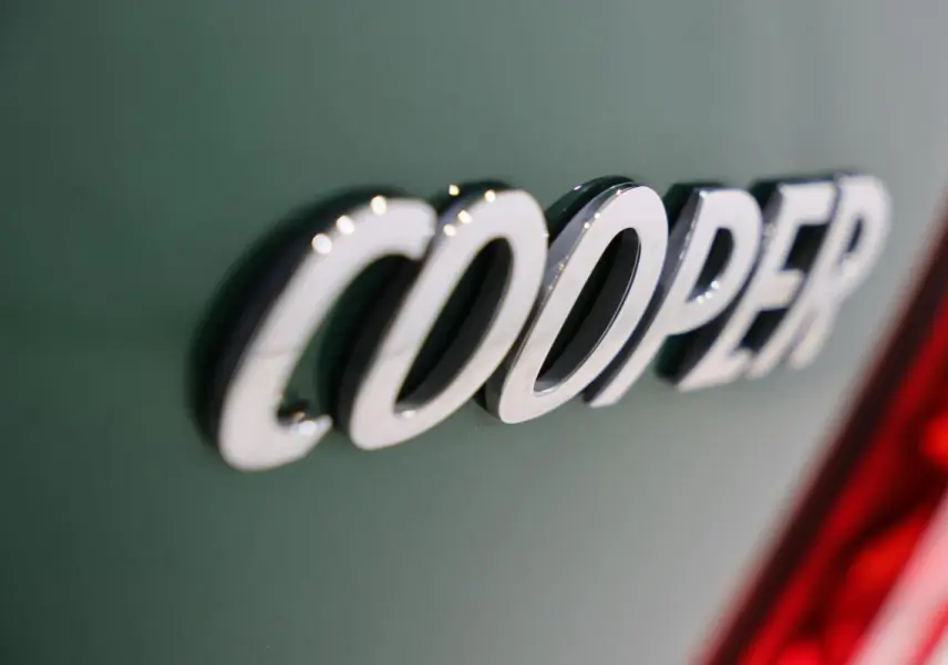 Gros plan sur l’inscription chromée Cooper sur la carrosserie vert métallisé d’un MINI Countryman, près du feu arrière rouge.