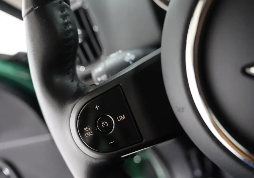 Gros plan sur les commandes de régulateur de vitesse au volant noir d’un MINI Countryman vert métallisé.