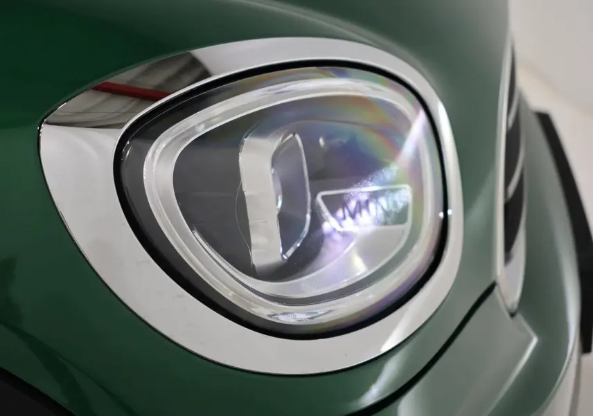 Gros plan sur le phare avant gauche d'une MINI Countryman vert métallisé avec contour chromé.