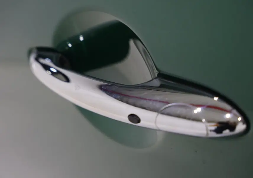 Poignée de porte chromée en gros plan sur une MINI Countryman vert métallisé, côté droit du véhicule.