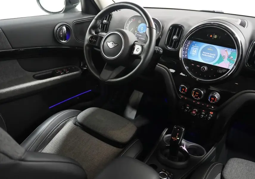 Vue intérieure côté conducteur du MINI Countryman 2021 avec tableau de bord noir, écran central rond et éclairage d'ambiance bleu.