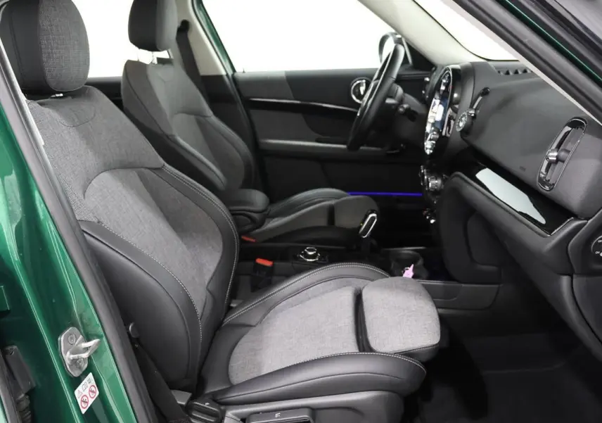 Intérieur avant droit d'une MINI Countryman vert métallisé, sièges tissu gris et cuir noir avec console centrale visible.