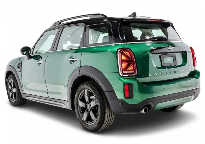 Vue 3/4 arrière droit d'une MINI Countryman vert métallisé avec toit noir et feux arrière Union Jack allumés.