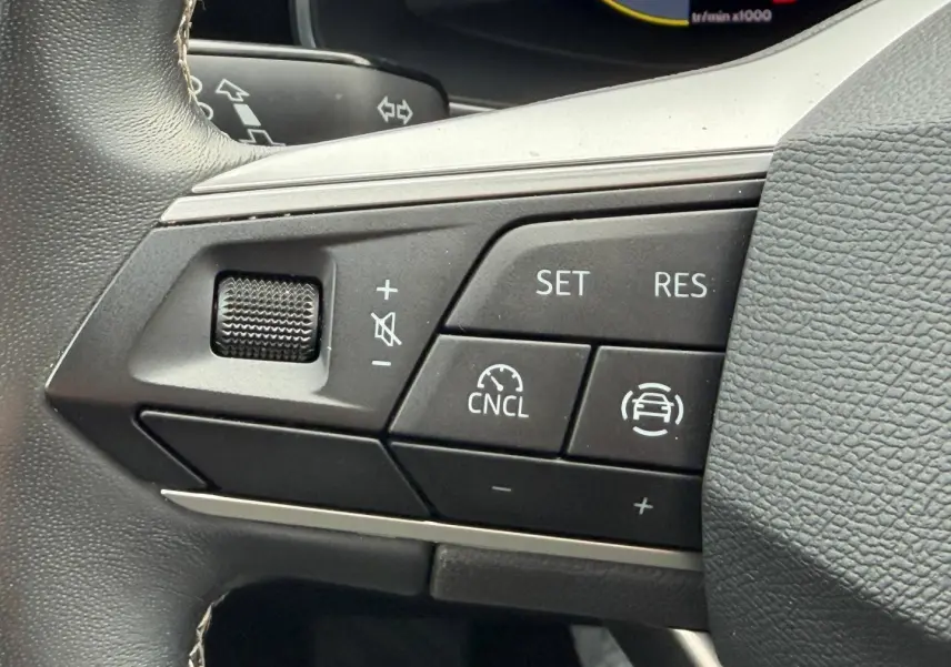 Gros plan sur les commandes du volant cuir multifonction du SEAT LEON gris Magnétique, boutons de régulateur de vitesse visibles.
