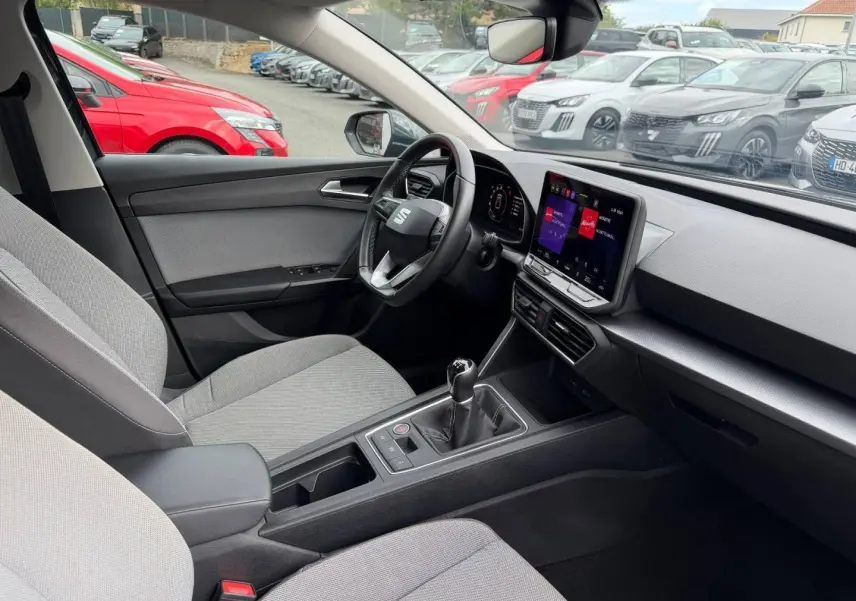 Vue intérieure côté conducteur du SEAT Leon 2025 gris, volant cuir multifonction et écran tactile central visible.