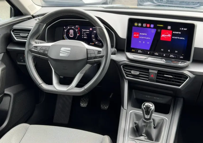 Vue intérieure du poste de conduite SEAT Leon 2025, volant cuir multifonction et écran tactile central lumineux.