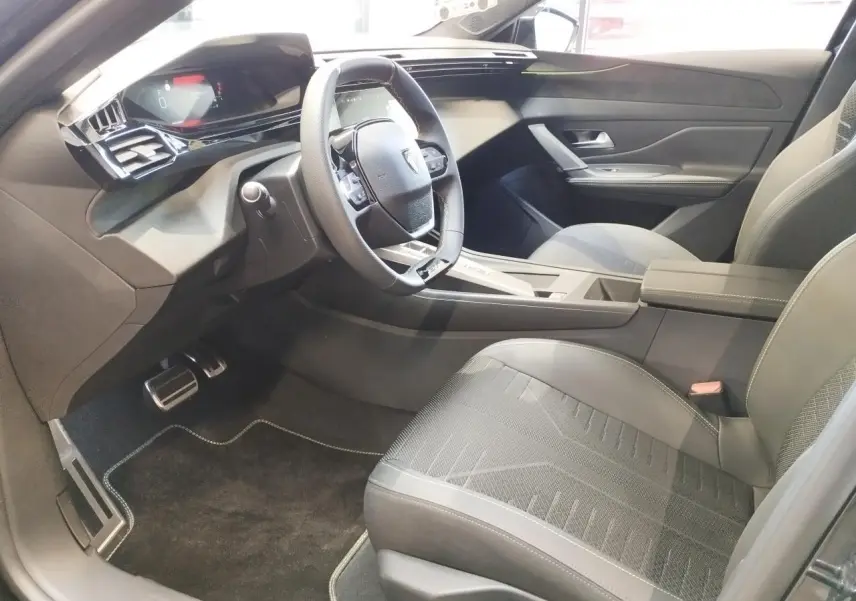 Intérieur avant droit de la Peugeot 308 1.2i Hybrid 2026 avec sellerie noire et volant compact GT cuir.