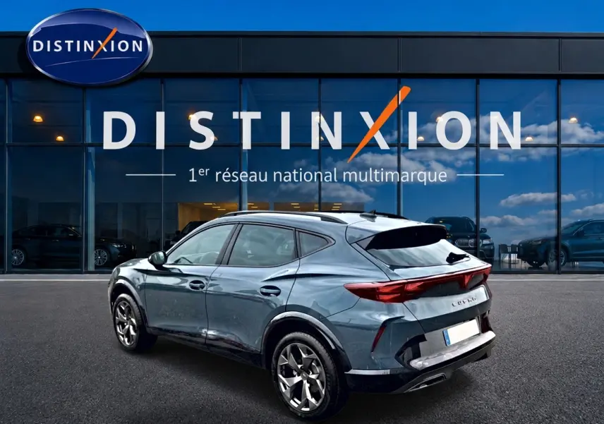 Vue 3/4 arrière droite d'un CUPRA Formentor bleu fjord avec feux arrière LED et jantes 18 pouces devant un showroom Distinxion.
