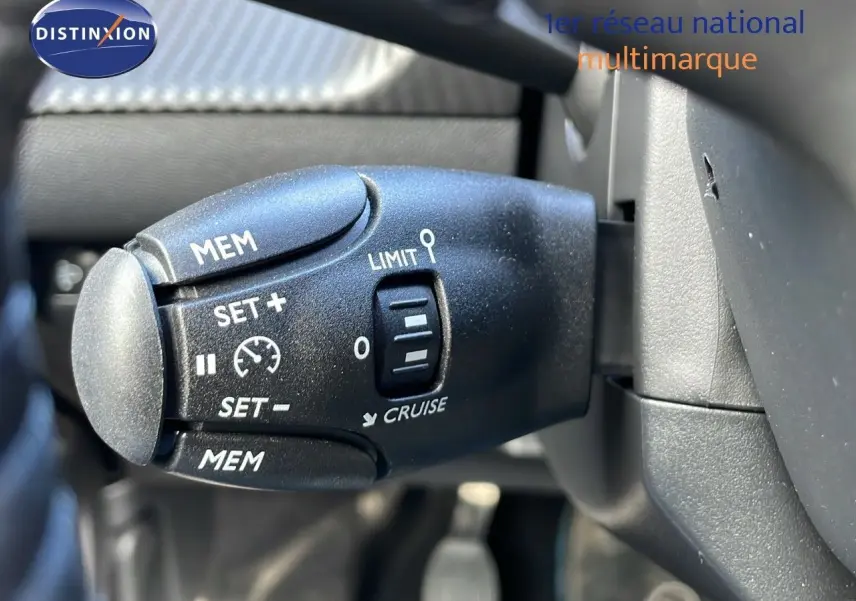 Gros plan sur la commande de régulateur de vitesse à gauche du volant dans l'habitacle du Peugeot 2008 blanc Okenite Metal.