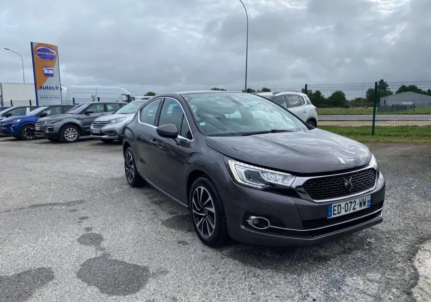 DS4 gris clair vue 3/4 avant droit sur parking avec calandre noire et jantes alliage distinctives.