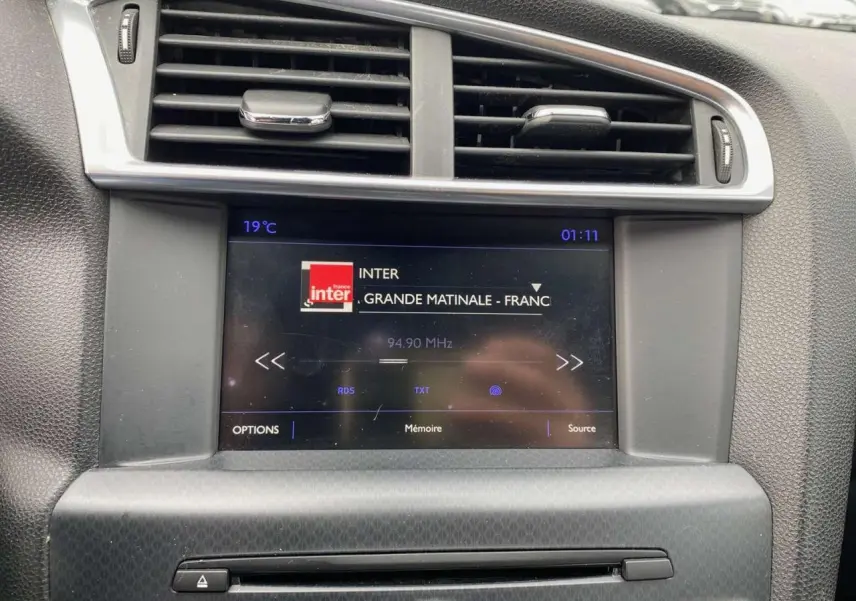 Écran tactile central affichant la radio dans l'habitacle du DS4 gris clair, vue rapprochée du tableau de bord.
