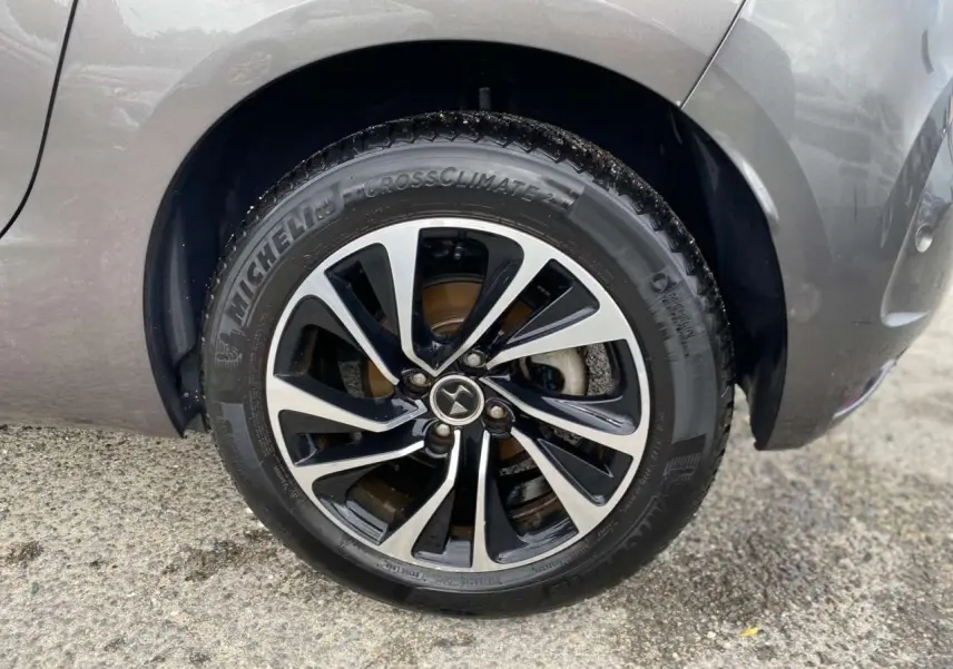 Gros plan sur la roue avant droite d'une DS4 gris clair, jante alliage bicolore et pneu Michelin CrossClimate.