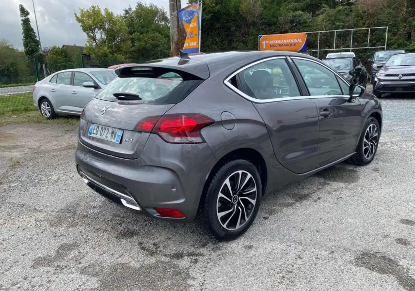 Vue 3/4 arrière droite d'une DS4 gris clair avec jantes alliage et feux arrière LED dans un parking extérieur.