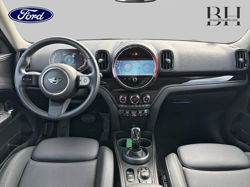 Vue intérieure avant du tableau de bord et volant noir du MINI COUNTRYMAN Cooper 2023 avec écran tactile rond central et sièges similicuir Carbon Black.