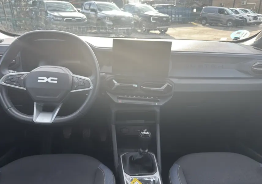 Vue intérieure frontale du tableau de bord du Dacia Duster 2025, volant cuir et levier de vitesse manuel visibles.