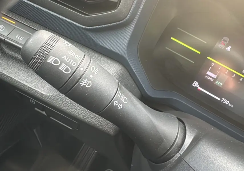 Gros plan sur la commande des phares et clignotants du tableau de bord du Dacia Duster 2025, intérieur noir.