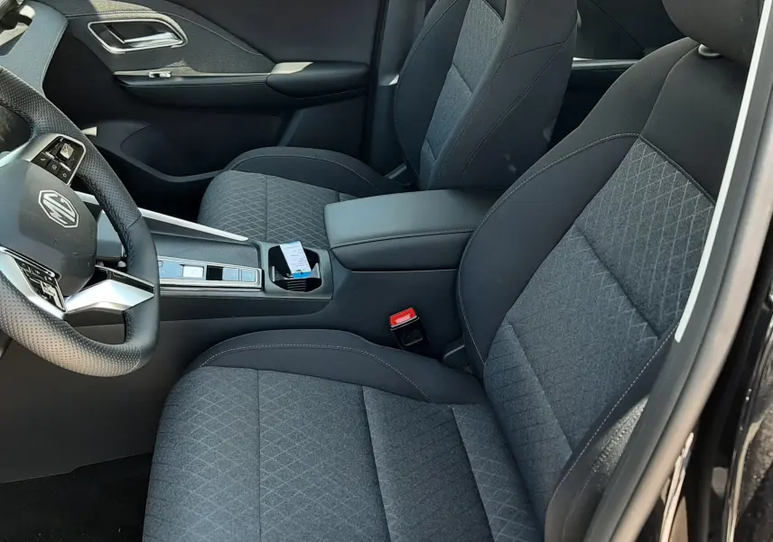 Vue intérieure côté conducteur du MG ZS 1.5L Hybrid+ 2026 avec sièges tissu gris et console centrale noire.