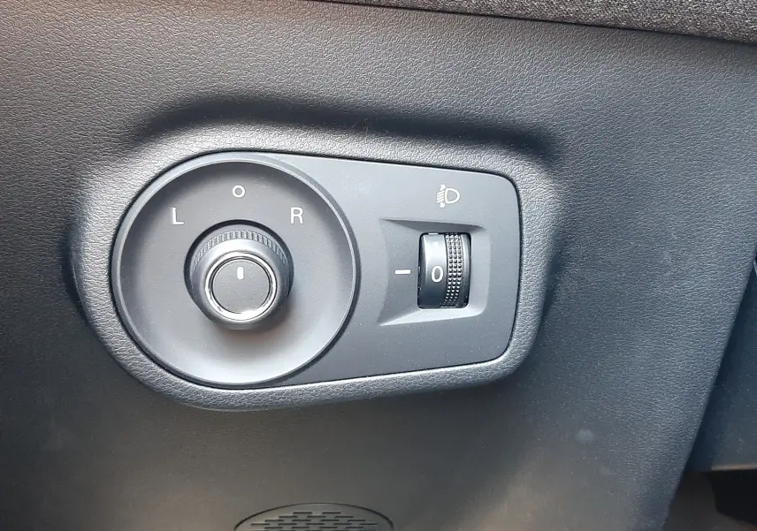 Gros plan sur les commandes de réglage des rétroviseurs et des phares, sur panneau noir intérieur d'un MG Motor ZS Pebble Black.