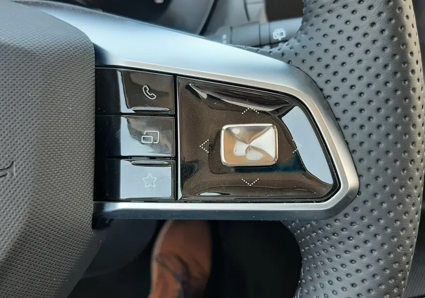 Gros plan sur les commandes noires et argentées au volant perforé du MG MOTOR ZS hybride, côté gauche.