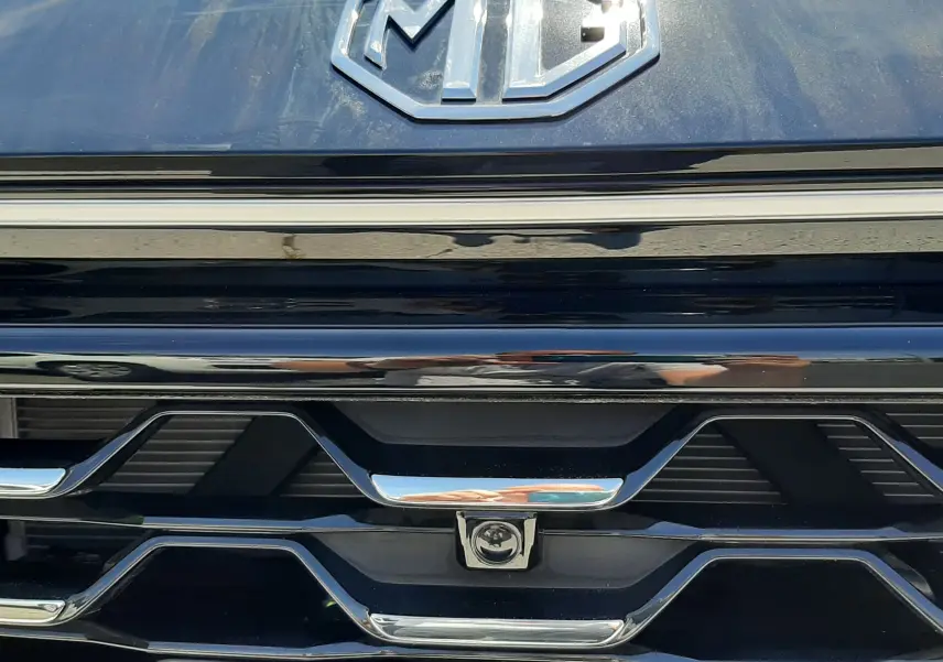 Gros plan sur la calandre noire Pebble Black Metal du MG ZS 1.5L Hybrid+ 197ch avec logo MG chromé et détails chromés.