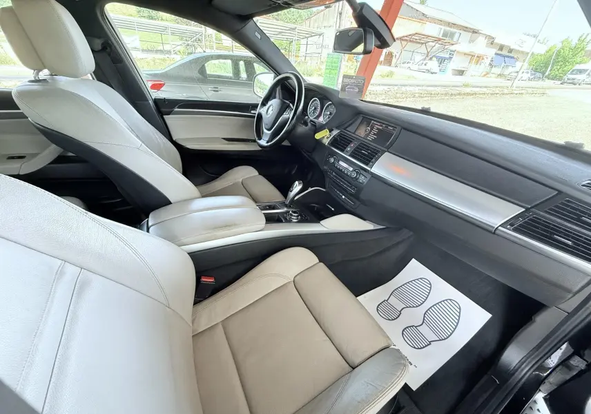 Vue intérieure côté passager d'une BMW X6 2011 avec sièges cuir beige et tableau de bord noir.