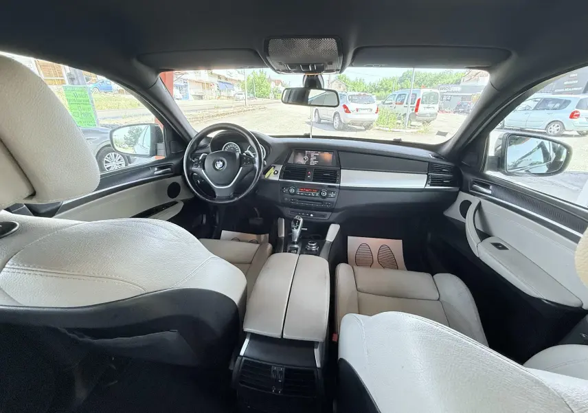 Vue intérieure avant du BMW X6 2011, sièges cuir clair et tableau de bord noir avec console centrale moderne.