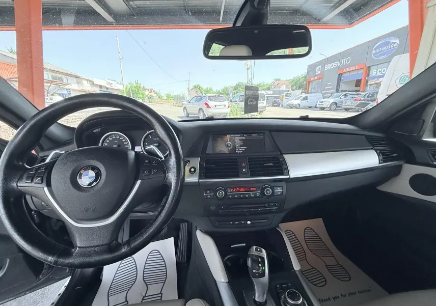 Vue intérieure du poste de conduite de la BMW X6 noire, avec volant, tableau de bord et console centrale visibles.