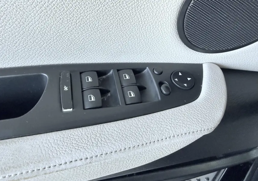 Gros plan sur les commandes des vitres électriques et rétroviseurs sur la portière intérieure en cuir clair du BMW X6 noir.