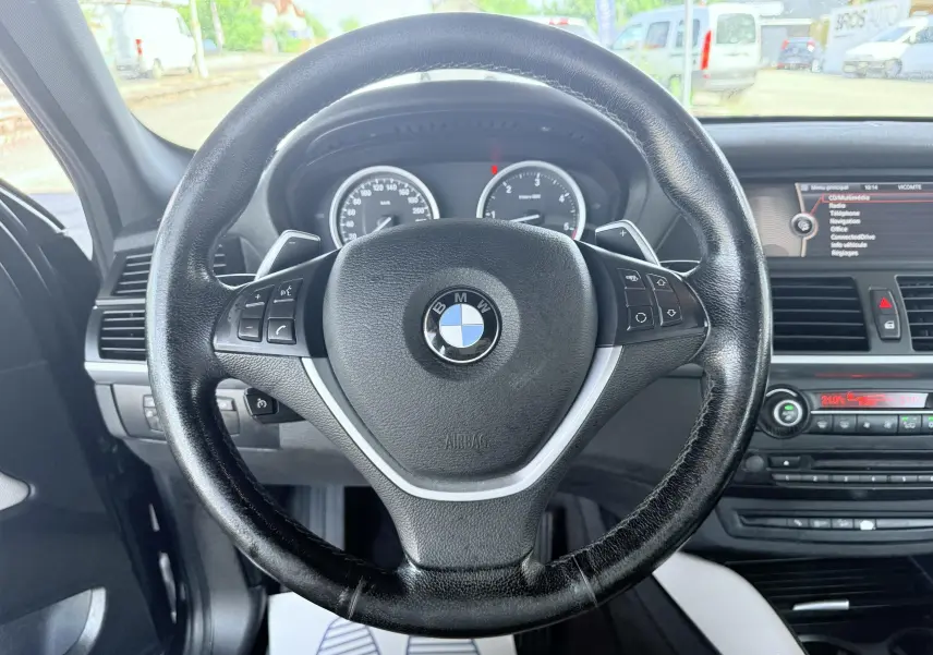 Vue intérieure centrée sur le volant noir de la BMW X6 2011 avec tableau de bord et écran multimédia visibles.