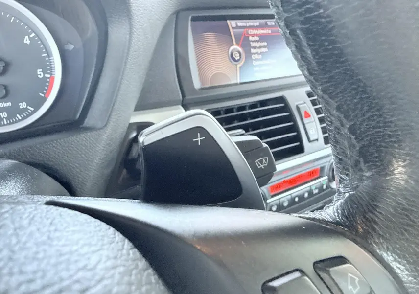 Gros plan sur la palette de changement de vitesse côté droit du volant cuir noir du BMW X6, avec tableau de bord et écran multimédia en arrière-plan.