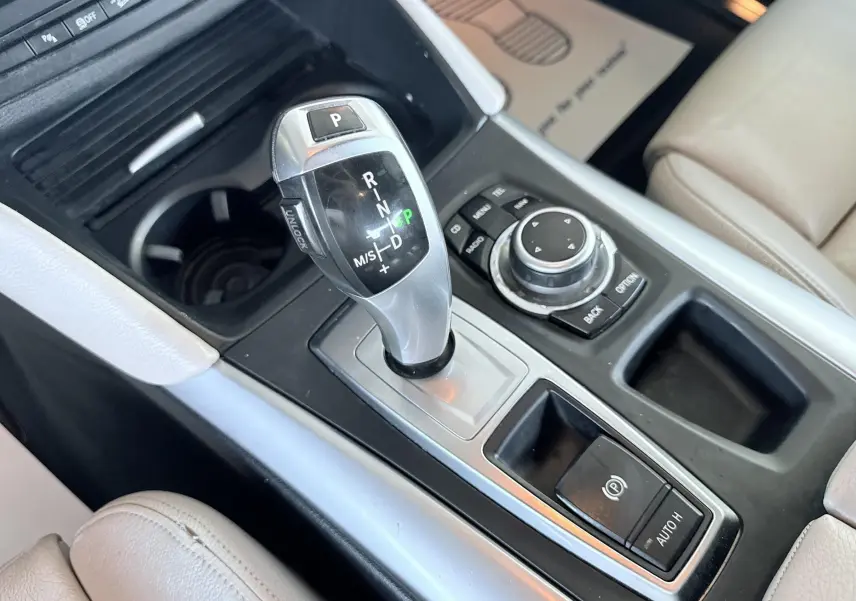 Gros plan sur la console centrale avec levier de vitesse automatique et commandes du BMW X6 noir, intérieur cuir beige.