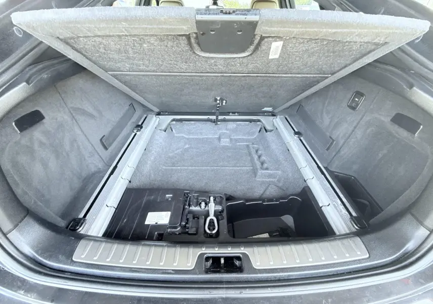 Coffre ouvert vu de l'arrière d'un BMW X6 noir, montrant le compartiment de rangement sous le plancher.