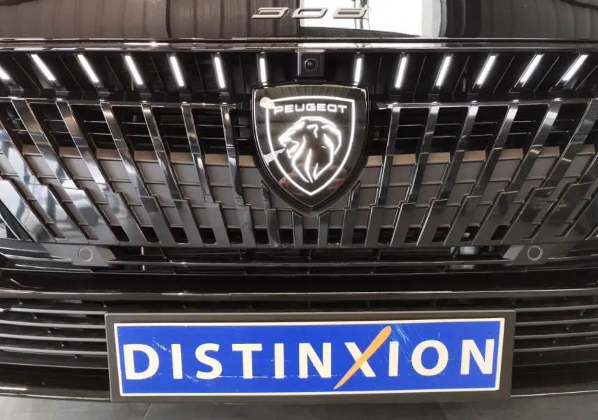 Gros plan sur la calandre noire métallisée de la Peugeot 308 Hybrid 2026 avec logo Peugeot illuminé et plaque Distinxion.