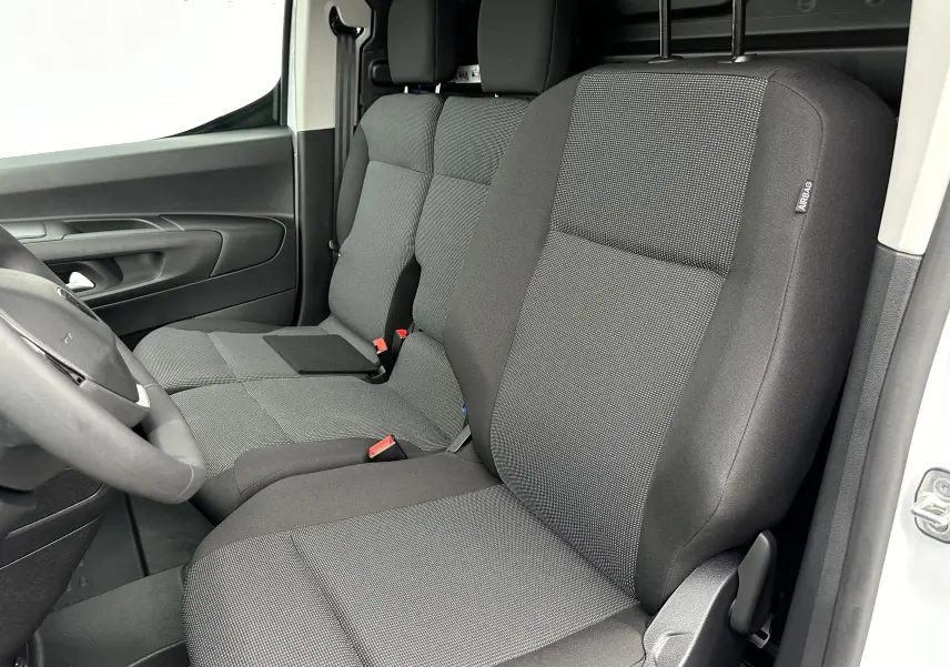 Vue intérieure côté conducteur du Peugeot Partner Fourgon blanc 2024, sièges tissu gris foncé avec appuie-tête intégrés.