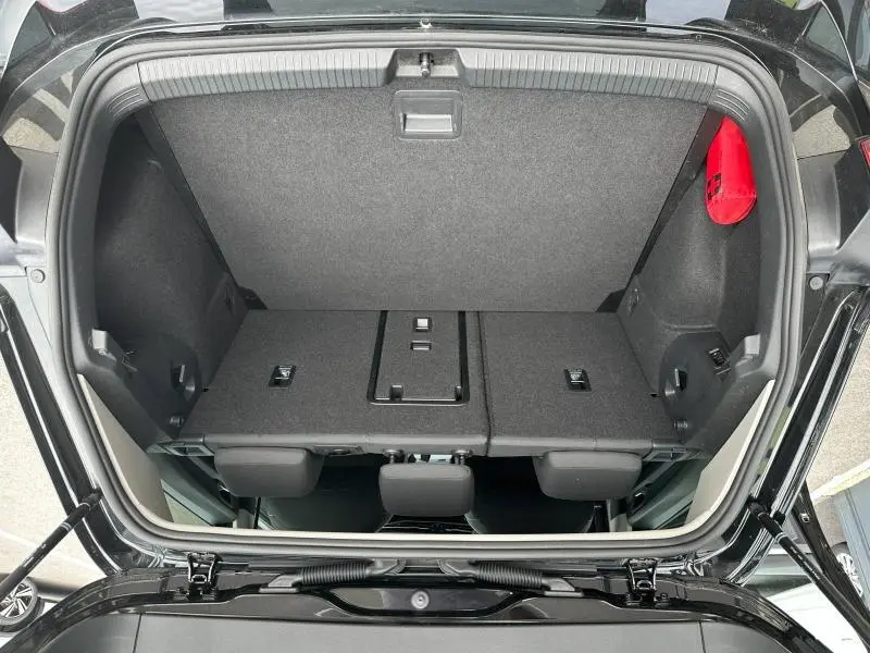 Coffre ouvert vu de dessus d'une Volkswagen Golf 1.5 eTSI noir intense nacré avec banquette arrière rabattue et trousse de secours rouge.