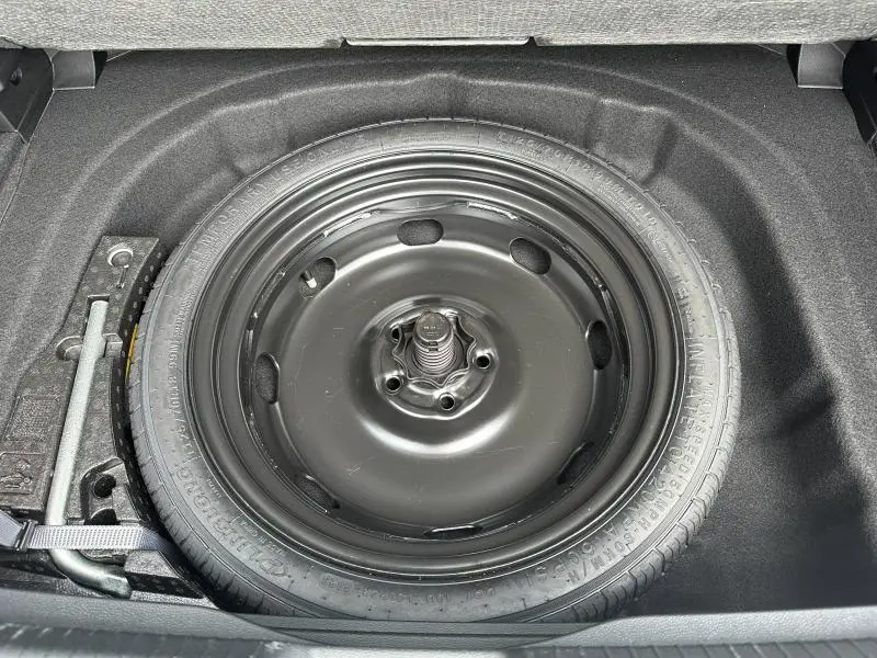 Vue rapprochée du pneu de secours noir dans le coffre d’une Volkswagen Golf 2024 Style Noir Intense nacrée.