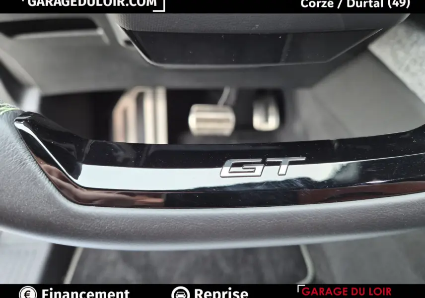 Gros plan sur le bas du volant noir avec logo GT et pédales en aluminium du Peugeot 3008 blanc 1.2 Hybrid 145 GT.