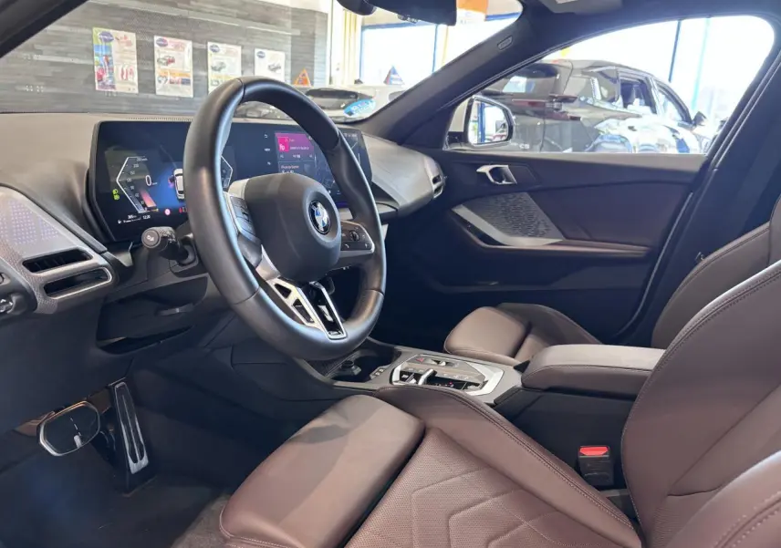 Vue intérieure côté conducteur de la BMW Série 1 120d M Sport 2025 avec volant multifonction et sellerie cuir marron.