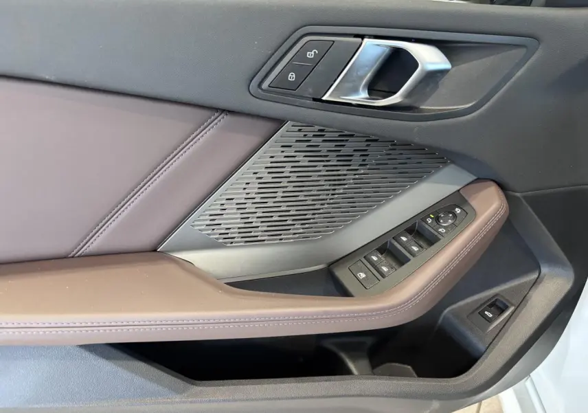 Détail de la porte côté gauche d’une BMW Série 1 120d M Sport 2025, avec garniture marron et commandes de vitres.