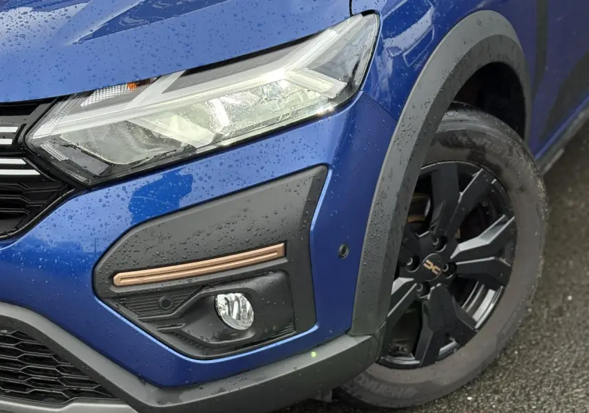 Gros plan sur l'avant droit bleu Iron du Dacia Sandero Stepway 2025, avec phare LED et jante alu noire distinctive.