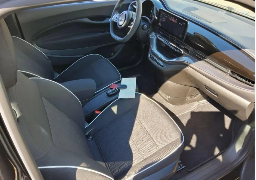 Vue intérieure côté conducteur de la Fiat 500 électrique 2024 avec sellerie tissu noir et écran tactile central.
