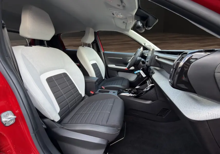 Vue intérieure côté conducteur de la Citroën C3 rouge 2026, sièges bicolores gris et noir, tableau de bord moderne avec écran tactile.