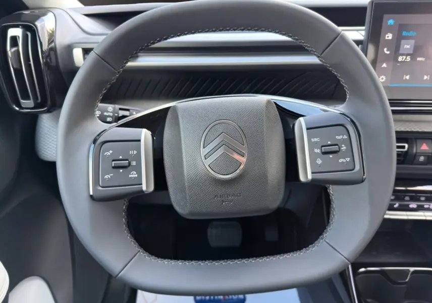 Vue rapprochée du volant cuir multifonctions de la Citroën C3 Hybride 110 MAX avec tableau de bord et écran tactile visible.