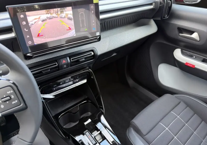 Vue intérieure côté passager de la Citroën C3 hybride rouge 2026, avec écran tactile affichant l’aide au stationnement arrière.