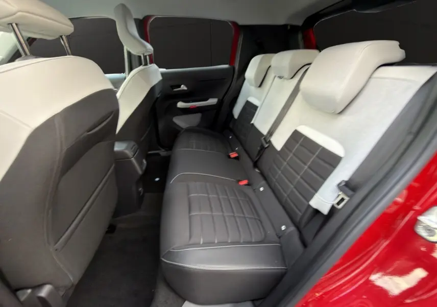 Vue intérieure arrière côté droit de la Citroën C3 hybride rouge, montrant la banquette bicolore noire et beige.