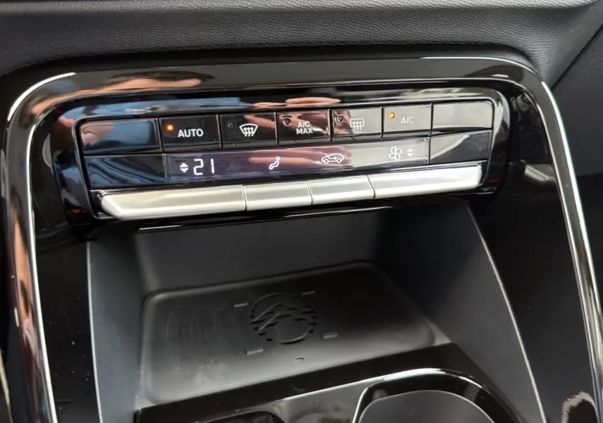 Gros plan sur la console centrale noire de la Citroën C3 hybride rouge, avec commandes climatisation et zone de recharge par induction.