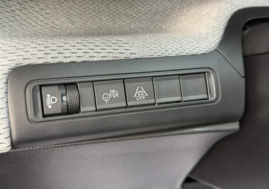 Gros plan sur les commandes de réglage des phares et d'aide à la conduite dans une Citroën C3 hybride rouge.